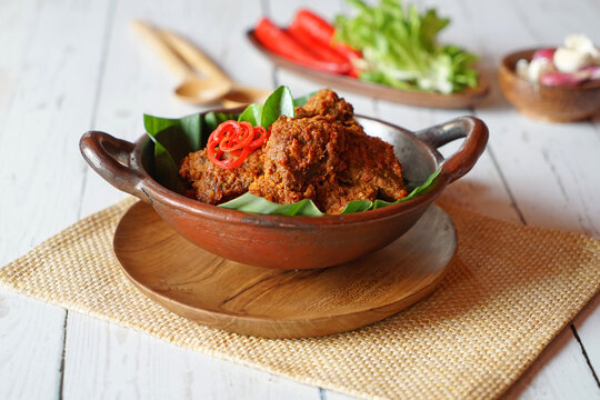 Traditional Indonesian spicy beef rendang served in a rustic clay bowl with banana leaves garnish on wooden table background. Famous Padang cuisine from Indonesia with rich spices and authentic homema