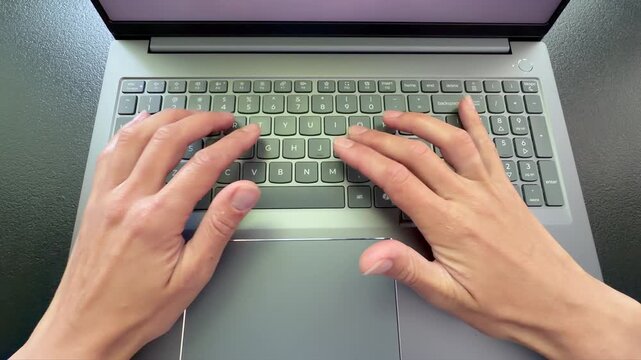 Top-down video captures a close-up view of a person's hands typing on a modern, silver laptop. Typing skills