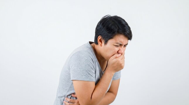 A man feeling sick and holding his hand to his mouth, appearing to be nauseous or about to vomit, with a plain white background.