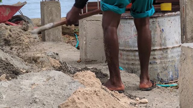 Construction workers transfer freshly mixed cement mortar into a wheelbarrow at an active building site. Ideal for construction, masonry, infrastructure development, and teamwork concepts.