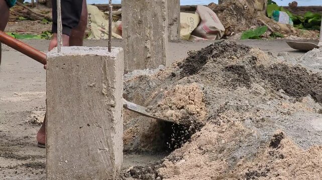 Close-up footage of a construction worker mixing sand and cement with a shovel at a building site. Ideal for masonry, concrete preparation, construction materials, and infrastructure development conce