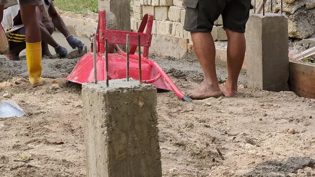 Construction workers transport wet mortar using a wheelbarrow at an active building site. Ideal for construction workflow, masonry work, building materials, and infrastructure development concepts.