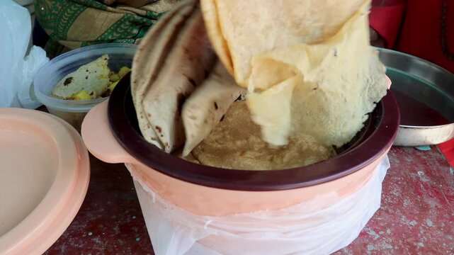 Raw video footage of poori, roti and traditional aloo ka gutka being distributed for lunch to temple beggars and visitors in rural Uttarakhand, India. Religious food service atmosphere.
