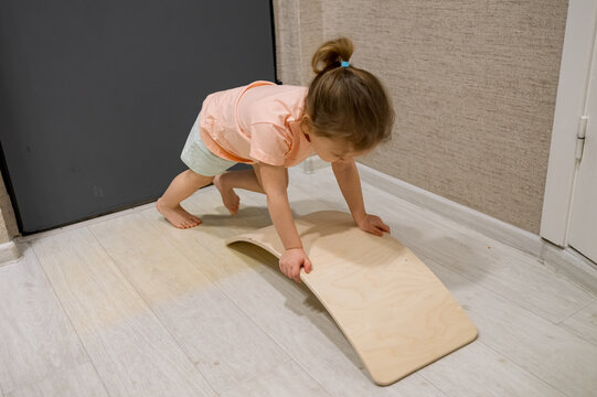 Little child playing on a wooden balance board, crawling and carefully learning to balance, developing gross motor skills and coordination playfully at home