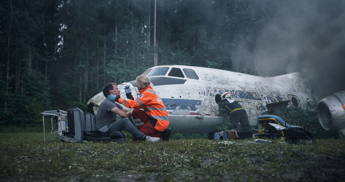Paramedics Treat an Injured Survivor Beside a Smoke-filled Airplane Wreck in a Forest, While Firefighters Work Around the Damaged Fuselage, Scattered Seats, and Debris During Crash Rescue Operations.