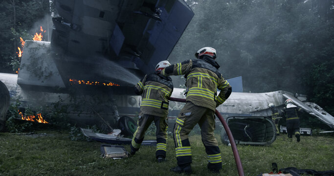 Firefighters Advance a Hose Line Beside a Downed Airplane in a Wooded Crash Zone, Tackling Flames and Smoke While Securing Wreckage for Rescue Access, Survivor Evacuation During Emergency Response