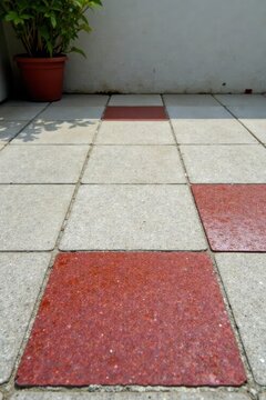 A potted plant sits beside a patio with a geometric pattern of gray and reddish-brown square tiles.