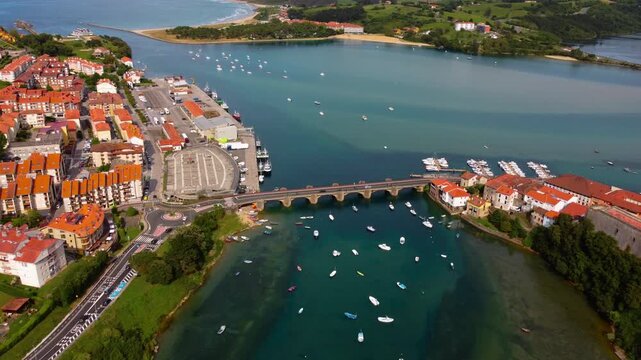 Top down aerial view of Barquera Bridge in San Vicente de la Barquera, showing colorful fishing boats moored in the turquoise estuary water in Cantabria, Northern Spain. High quality 4k footage