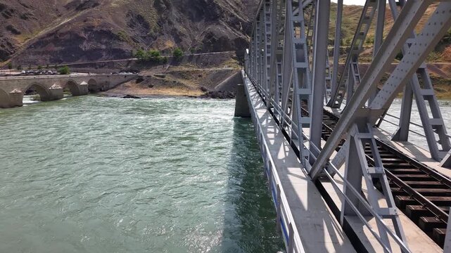 Cinematic 4K drone slowly moving backward parallel to railway bridge over river. Smooth reverse motion, detailed structure view, travel and architecture scene.