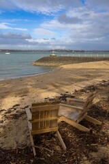 Obraz premium Two empty wooden chairs sit on the beach in Devonport, Auckland, New Zealand, providing a peaceful place to enjoy the harbor and calm sea.