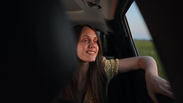 Woman smiles while talking to passenger inside car. Female converses with person during vehicle trip. Girl speaks and smiles in automobile. Woman having conversation while sitting in car.