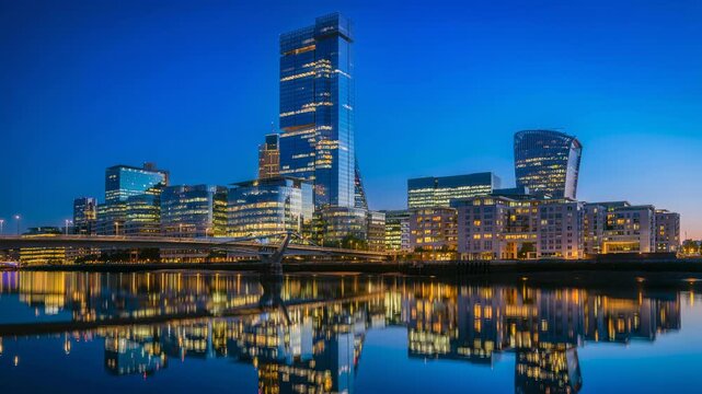 Modern city skyline at dusk with illuminated office buildings and river reflections in urban landscape