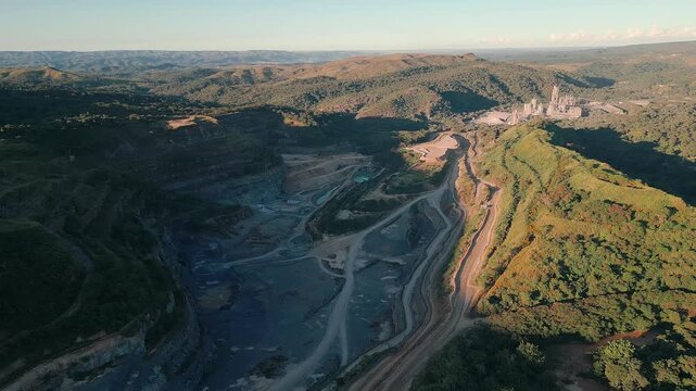 Open pit rare earth mining valley and mineral processing infrastructure near Bras&iacute;lia, Federal District, Brazil, cutting native Cerrado hills with visible haul roads and extraction zones, aerial