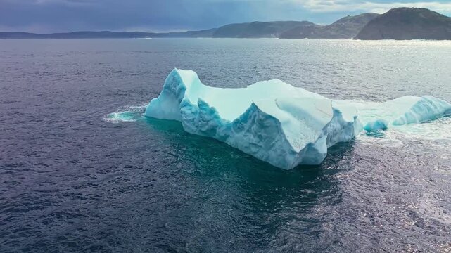 Drone footage of chunky iceberg floating off rocky St Johns coastline under cloudy skies