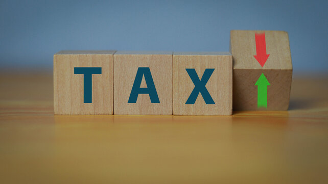 Wooden blocks spelling TAX with red downward and green upward arrows on stacked cubes. Concept of taxation, tax increase or reduction, government policy, business finance, and economic impact.