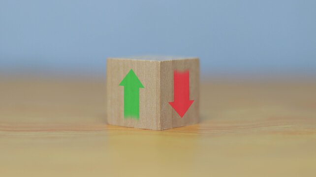 Wooden cube displaying green upward arrow and red downward arrow on opposite sides. Concept of business growth and decline, market trends, risk management, investment performance, and economic 