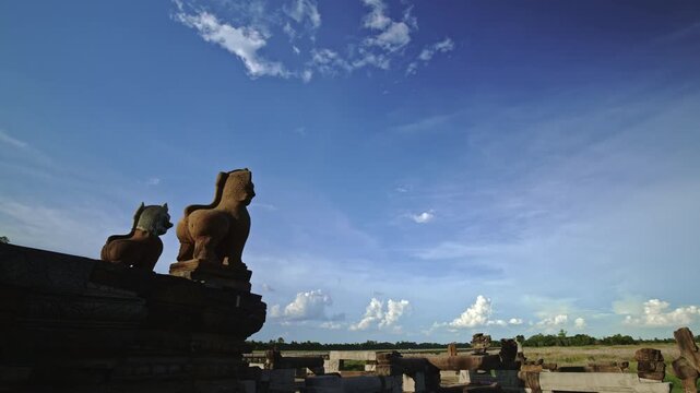 Aincient Angkorian sandstone lion statues overlook baray lake filled with grass at the start of rainy season. Motion control dynamic movement time lapse.