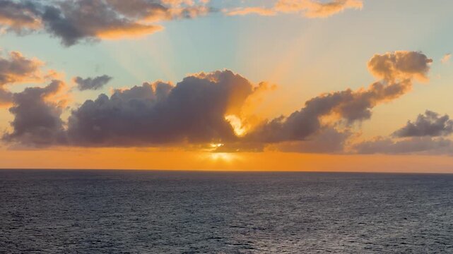 Static wide shot of a vivid tropical sunset over the Caribbean Sea with deep orange and golden light illuminating dramatic cloud formations above a calm ocean horizon. Shot on iPhone 17 Pro.