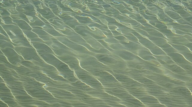 Close-up of shallow crystal-clear water with rippling light patterns over sandy seafloor at San Lorenzo beach, Gijon.