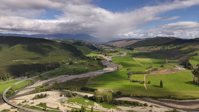 Aerial drone shot of Motueka River flowing past green farms with shadows of clouds in Tasman region in New Zealand,