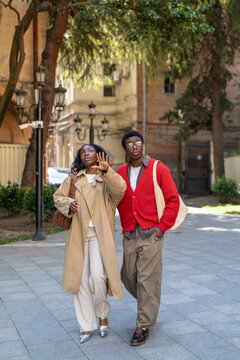 Fashionable curious african american man and woman spending weekend walking in city together, stylish positive black male and female date on daily walk, talking and looking around in downtown