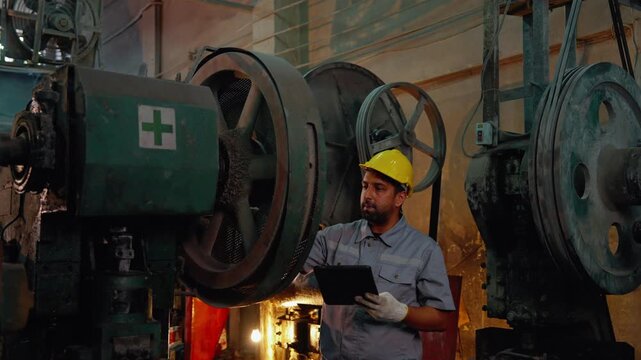 Industrial maintenance technician using a digital tablet to inspect heavy machinery in a factory environment. Smart manufacturing and predictive maintenance concept.

