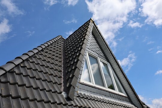Dark tile roof with dormer window against blue sky