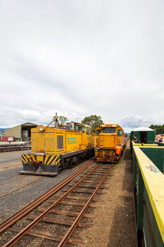 Two yellow diesel locomotives stand side by side in the Waihi rail yard, with a worker in high‑visibility gear attending to one of the engines