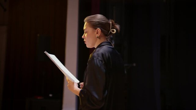 Actors rehearsing dramatic script readings on a dimly lit theater stage, focusing on performance, concentration, and expressive interpretation during a live practice session