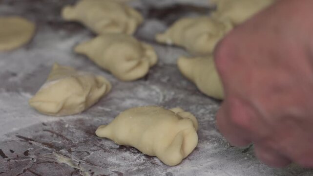 High angle close-up of handmade pierogi dumplings on a floured wooden surface, ready for cooking. Traditional Eastern European homemade dough pockets filled with savory ingredients.