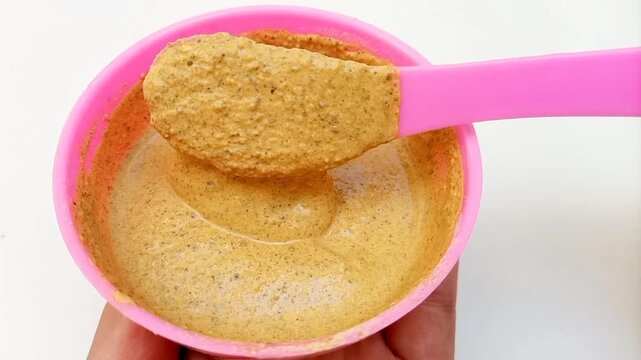 Traditional Ayurvedic Ubtan Powder Mixing Process in Pink Plastic Bowl with Mixing Spoon Isolated on White Background