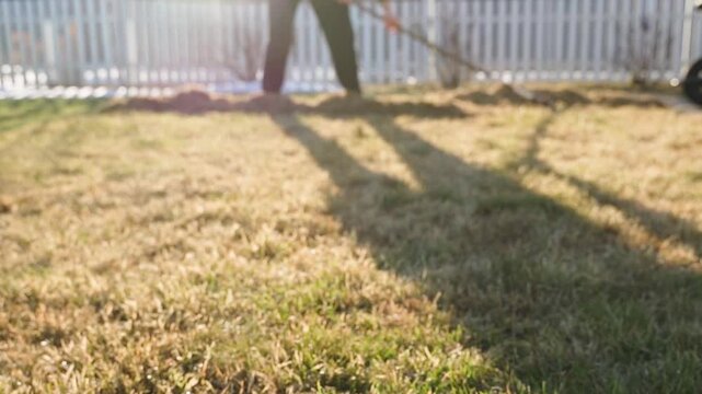 Person raking lawn in backyard on sunny spring morning with blurred foreground