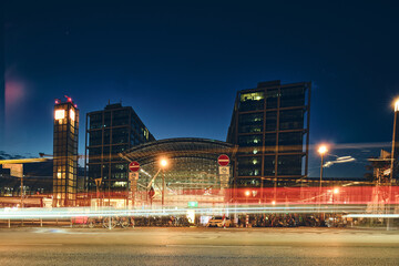 Fototapeta premium Nighttime urban scene featuring a contemporary glass building complex with glowing interior lights, long exposure traffic light trails, and a dark blue sky