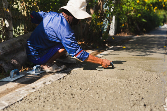 Construction worker crouching on a roadside to smooth wet cement using a hand trowel