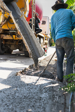 Construction worker leveling fresh wet cement pouring from a mixer truck