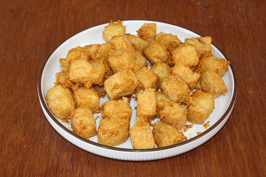 Crispy golden brown fried tofu cubes on plate over wooden background