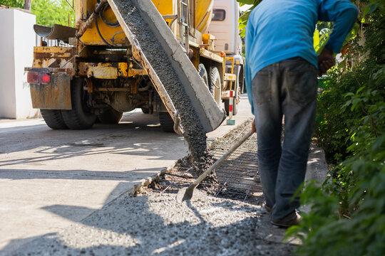 Construction worker leveling fresh wet cement pouring from a mixer truck