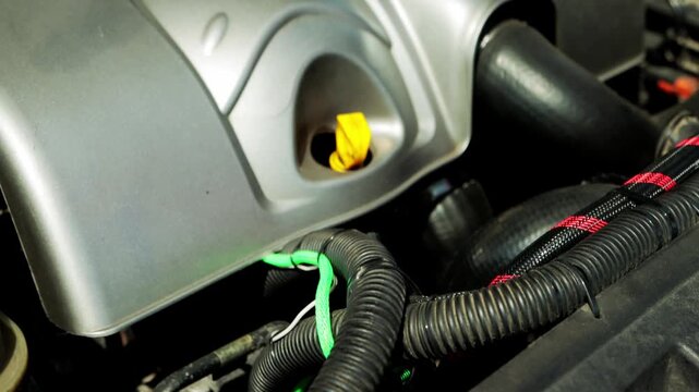 Detailed look at modern automobile engine bay revealing silver engine components, prominent yellow oil dipstick, and intricate network of corrugated hoses and bundled wires crucial for vehicle operati
