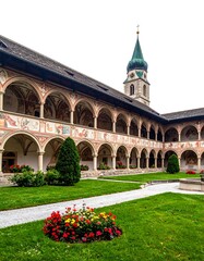 Obraz premium A serene courtyard with a lush lawn, vibrant flowers, and a historic building featuring arched walkways and a tower