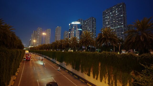 Blue hour view of the Trung Hoa underpass in Hanoi with illuminated traffic, palm trees, and high-rise residential buildings.