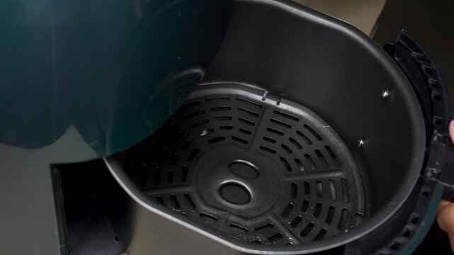 Woman hand using Red greasing silicon brush butter on air fryer basket, concept for cooking and modern home kitchen appliance.
