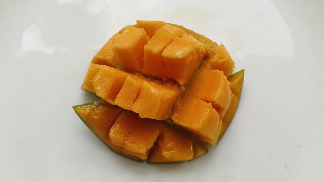 Mango fruit sweet juicy yellow ripe flesh slice and cut into cube piece isolated on white plate background. Closeup top spinning or rotation view of sweet delicious and tasty fresh mango chunk.