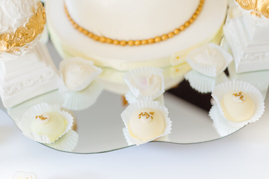 Elegant white and gold wedding cake with petit fours on mirrored dessert table for celebration