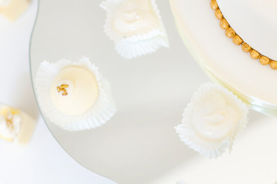 Elegant white wedding desserts and gold-accented truffles on mirrored serving platter for reception