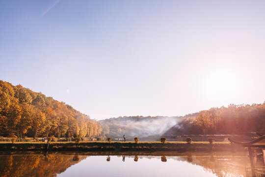 Couple standing by tranquil lake at sunrise with autumn trees and misty reflections