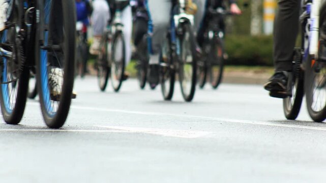 Motion blur of group bike ride with many participants cycling on wet street pavement, low angle view emphasizing movement of bicycle wheels and legs of riders, outdoor sport activity.