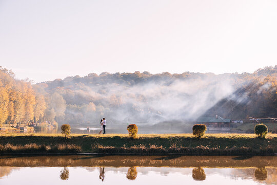 Romantic couple embracing by a misty lake at sunrise with autumn trees and reflections