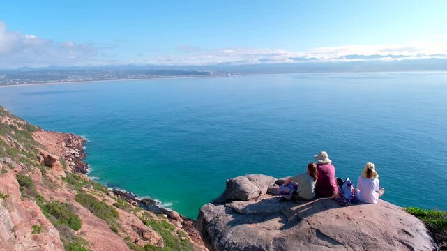 Family picnic atop boulder on cliff overlooking ocean at Robberg marine reserve
