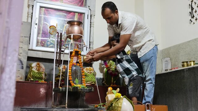 indian father and son offering shivling abhishek ritual at shiva temple during religious ritual