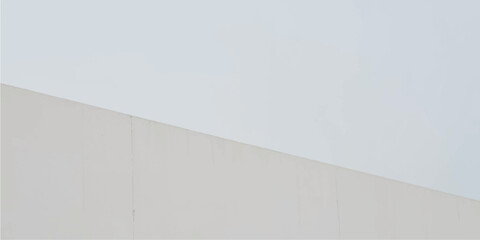 A rough concrete wall with a vintage textured surface stands against a bright blue sky to create a minimalist architectural design background © Alpha Designs
